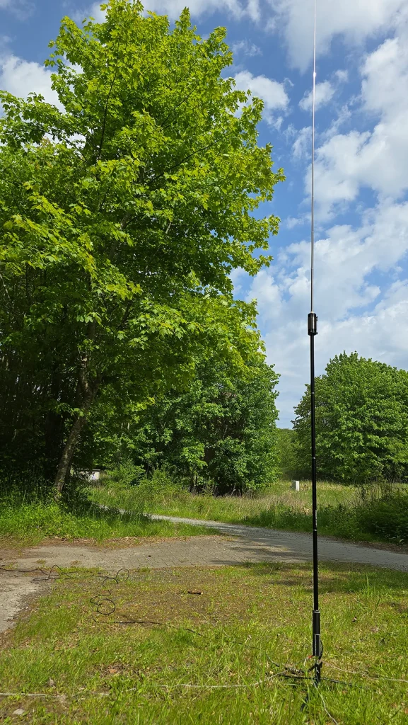 JPC-12 Antenne rechts im Bild. Links ein Baum blauer bewölkter Himmel, Sonnenschein.