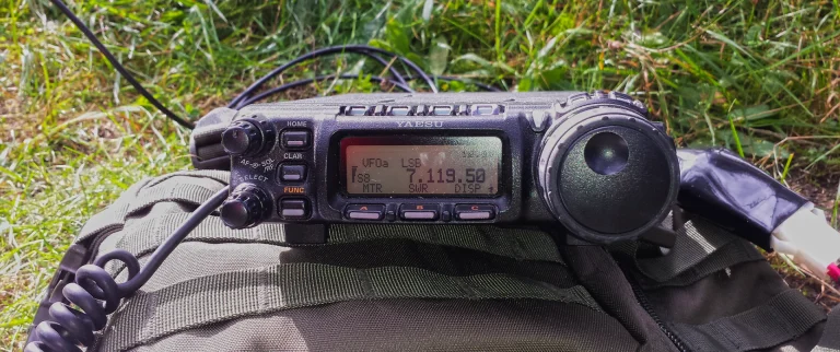 Yaesu FT-857 kurzwellentransceiver in Nahaufnahme auf einem olivgrünen Rucksack auf einer Wiese liegend.