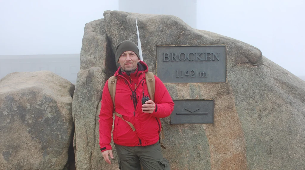 DO4KAI auf dem Brocken im Harz, vor dem Gipfelschild am Fels bei nebligen Wetter.